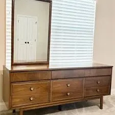 Sale Photo Thumbnail #21: Mid-century modern walnut triple dresser with matching wood-framed wall mirror, featuring tapered legs and brass knob pulls.