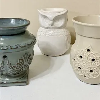 Sale Photo Thumbnail #37: Three ceramic wax warmers, including a blue-grey urn style, a white owl figure, and a cream-colored vessel with cutout details.