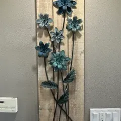 Sale Photo Thumbnail #53: Rustic wall art featuring blue-green metal flowers and leaves mounted on a vertical wooden plank backing.