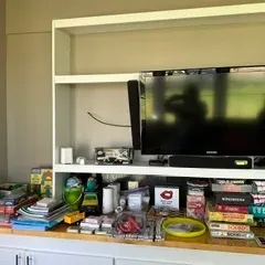 Sale Photo Thumbnail #57: Samsung flat-screen television with soundbar, housed in a white wooden shelving unit alongside various board games, toys, and household items.