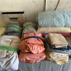Assorted vintage bed linens and blankets in various colors, folded and organized on a table.
