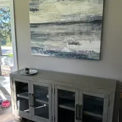 Sale Photo Thumbnail #39: Contemporary gray wood sideboard with four glass-front doors and metal hardware, paired with a large abstract canvas painting in muted tones.