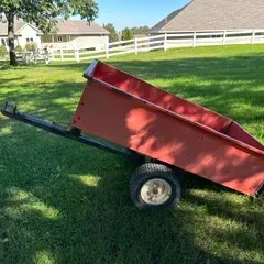 Red painted wooden utility cart with a steel frame and pneumatic tires, designed for towing behind a lawn tractor or ATV.