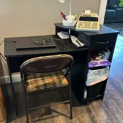 Sale Photo Thumbnail #59: Compact black laminate computer desk with a raised shelf, side drawer, and open storage cubbies, paired with a vintage plaid-cushioned folding chair.