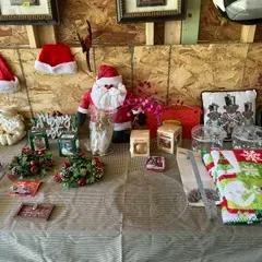 Assortment of Christmas decorations, including a plush Santa Claus figure, Santa hats, festive table linens, and holiday-themed...