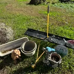 Assorted garden items including plastic planters, a dog figurine, a decorative bird planter, a welcome sign, and a yellow-handled lawn tool.