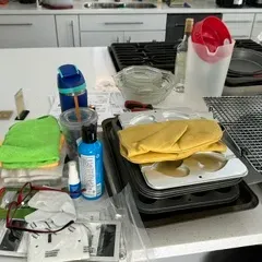 Sale Photo Thumbnail #41: Assorted kitchenware and household items, including baking pans, cooling racks, microfiber cloths, and a plastic pitcher, arranged on a kitchen island.