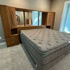 Sale Photo Thumbnail #31: Vintage oak king-size pier group headboard with integrated nightstands, overhead cabinets, and a mirrored back panel, shown with a modern mattress set.