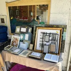 Sale Photo Thumbnail #22: Assortment of picture frames in various sizes, styles, and colors, displayed on a table alongside a large wood-framed wall mirror.