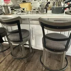 Sale Photo Thumbnail #40: Trio of modern farmhouse swivel barstools featuring gray upholstered seats with nailhead trim, weathered gray wood frames, and black metal accents.