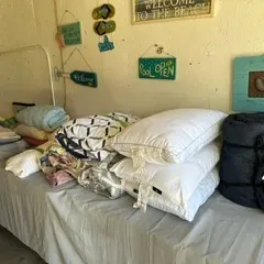 Sale Photo Thumbnail #21: Assorted bedding and linens, including pillows, blankets, and sheets, displayed on a table alongside beach-themed wall decor.