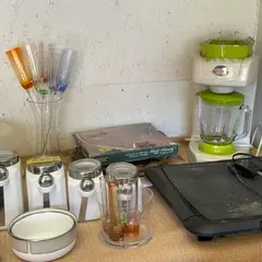 Assorted kitchenware including a white and green blender, a black electric griddle, three white canisters with silver lids, and colorful...