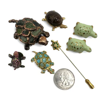 Sale Photo Thumbnail #102: Collection of vintage turtle-themed jewelry, including a stickpin, brooches, and small pins in various materials like enamel, rhinestones, and carved stone.