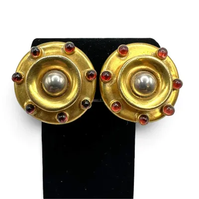 Sale Photo Thumbnail #130: Pair of vintage round clip-on earrings featuring a gold-tone finish, a central silver-tone dome, and red cabochon accents.