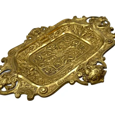 Sale Photo Thumbnail #80: Ornate brass or bronze vanity tray featuring intricate scrollwork, floral motifs, and a sculpted face detail on the border.