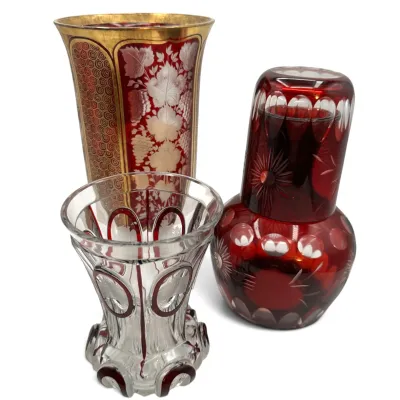 Sale Photo Thumbnail #44: Three pieces of vintage Bohemian ruby cut-to-clear glass, including a tall vase with gold-gilt accents, a small flared vase, and a tumble-up nightstand carafe set.