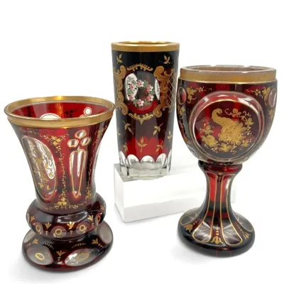 Sale Photo Thumbnail #45: Three pieces of Bohemian ruby cut-to-clear glass, including a vase, tumbler, and goblet, featuring intricate gold gilt detailing and hand-painted floral motifs.