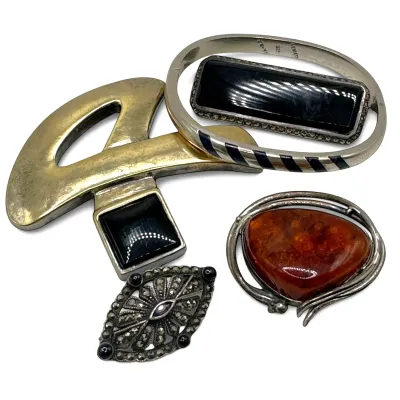 Sale Photo Thumbnail #120: Assortment of vintage jewelry including a large amber cabochon brooch, a marcasite eye-shaped brooch, a silver-tone bangle with black inlay, and a modernist brass and black stone pendant.