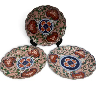 Sale Photo Thumbnail #7: Set of three Japanese Imari porcelain plates featuring scalloped rims and intricate floral patterns in rust, blue, and green tones.