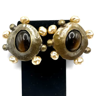 Sale Photo Thumbnail #132: Vintage brutalist-style clip-on earrings featuring hammered gold-tone metal, central oval tiger's eye cabochons, and faux baroque pearl accents.