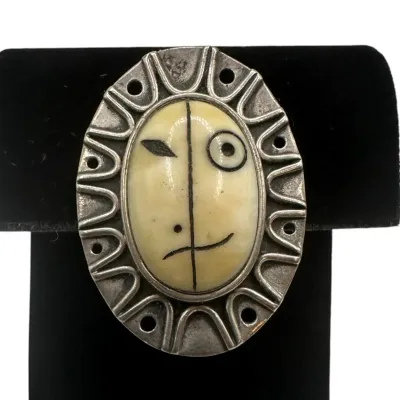 Sale Photo Thumbnail #146: Vintage modernist sterling silver and carved bone face brooch, featuring a stylized Picasso-esque portrait in an oval frame.