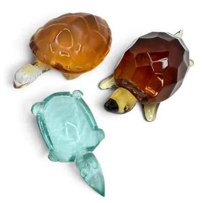 Sale Photo Thumbnail #21: Three vintage glass turtle figurines, including a faceted amber glass turtle, a smooth honey-colored glass turtle, and a light blue-green glass turtle.