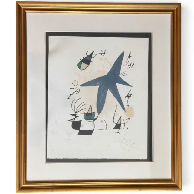 Sale Photo Thumbnail #175: Joan Miró abstract lithograph, featuring a central blue star shape and surrealist figures, signed and numbered in pencil, presented in a matted gold-finished frame.