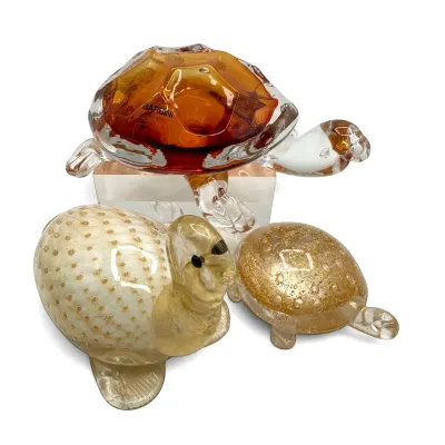 Sale Photo Thumbnail #24: Three vintage Murano art glass turtle figurines, including a Barbini Murano amber glass turtle on a clear block base, alongside two smaller gold-flecked and textured glass turtles.