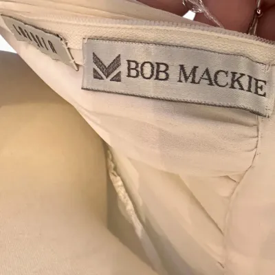 Sale Photo Thumbnail #177: Bob Mackie designer label sewn into a white garment, showing the brand name and logo.