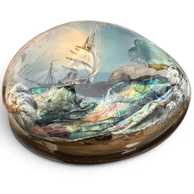 Sale Photo Thumbnail #91: Hand-painted abalone shell paperweight depicting a sailing ship navigating rough, iridescent waves under a clear resin dome.