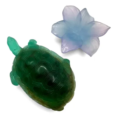 Sale Photo Thumbnail #34: Two decorative molded glass figurines, featuring a green sea turtle and a purple and blue flower, both with a frosted finish.
