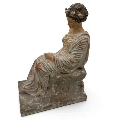 Sale Photo Thumbnail #54: Tanagra-style terracotta figurine depicting a seated woman in classical draped attire, showing a weathered, antiqued finish with remnants of paint.