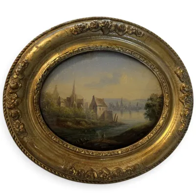 Sale Photo Thumbnail #63: Antique European school oil painting depicting a river landscape with a church and village, housed in an ornate oval gilt gesso frame.