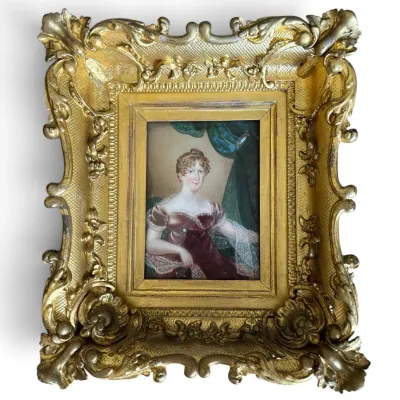 Sale Photo Thumbnail #60: Antique miniature portrait painting of a woman in a burgundy dress, housed in an ornate, heavily carved gilt gesso frame.