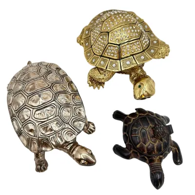 Sale Photo Thumbnail #84: Trio of decorative turtle figurines, including a gold-tone hinged trinket box accented with rhinestones, a silver-tone metal turtle, and a dark carved resin or wood turtle.