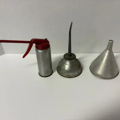 Sale Photo Thumbnail #62: Vintage metal oil cans and a funnel, including a red-handled thumb pump oiler and a classic dome-shaped oiler with a long spout.