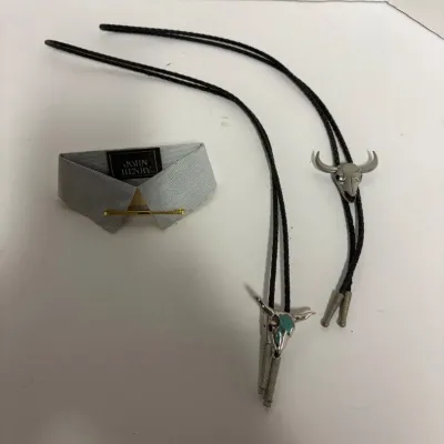 Sale Photo Thumbnail #4: Two Western-style bolo ties featuring steer skull slides, one with turquoise-colored inlay, shown alongside a vintage collar bar and fabric collar piece.