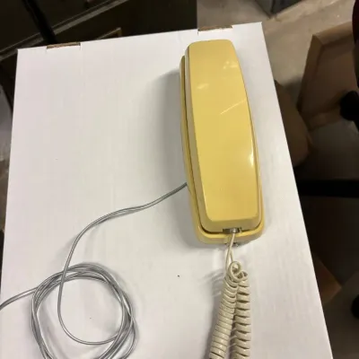 Sale Photo Thumbnail #38: Vintage yellow wall telephone with a coiled handset cord and straight line cord, showing some light wear.