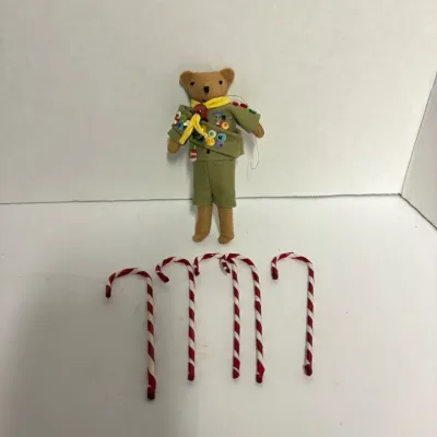 Sale Photo Thumbnail #8: Miniature Boy Scout teddy bear ornament wearing a green uniform with merit badges, accompanied by five small plastic candy canes.
