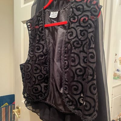 Vintage black flock-print vest with spiral motif hanging over a black skirt on a red hanger.