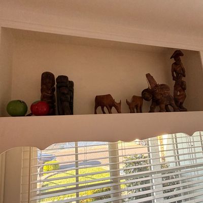 Sale Photo Thumbnail #28: Collection of hand-carved wooden figurines, including animals, human figures, and tiki-style carvings, displayed on a shelf above a window.