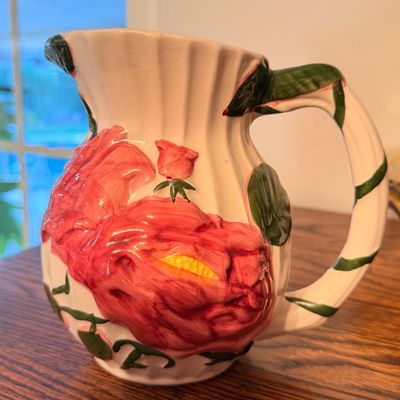 Sale Photo Thumbnail #77: Vintage ceramic pitcher featuring raised pink cabbage rose motifs, green vine handle, and fluted rim detail.