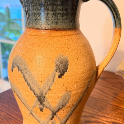 Sale Photo Thumbnail #106: Handcrafted studio pottery pitcher featuring a two-tone design with a dark greenish-gray neck and a textured ochre body accented by abstract brushed motifs.