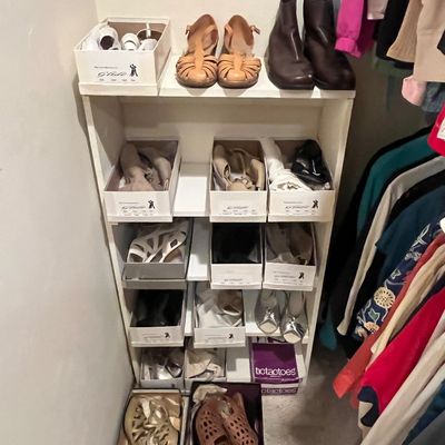 White wooden shoe rack filled with various boxed and unboxed women's dress shoes, sandals, and boots.