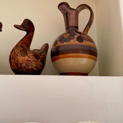 Sale Photo Thumbnail #31: Hand-painted Tonala Mexican pottery pitcher alongside a carved wooden duck figurine, displayed on a white shelf.