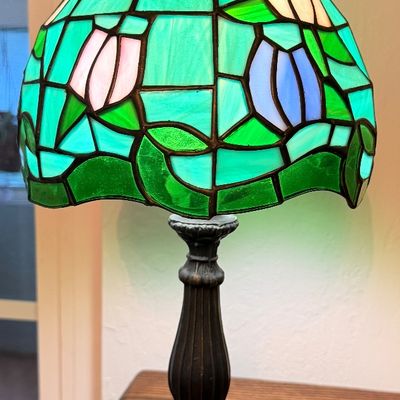 Sale Photo Thumbnail #74: Small Tiffany-style table lamp featuring a green leaded slag glass shade with colorful floral tulip accents on a dark metal base.