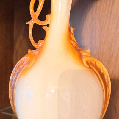 Sale Photo Thumbnail #75: Vintage ceramic decorative pitcher vase featuring a two-tone orange and cream glaze with an ornate, reticulated handle.