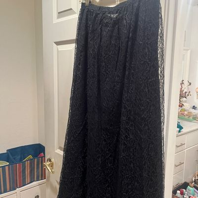 Black floral lace maxi skirt with an elastic waistband, hanging from a plastic hanger against a door.