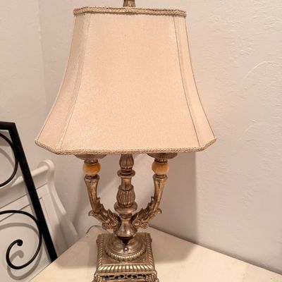 Sale Photo Thumbnail #46: Ornate traditional table lamp featuring a distressed gold-finished metal base with decorative scrollwork and a beige bell-shaped fabric shade.