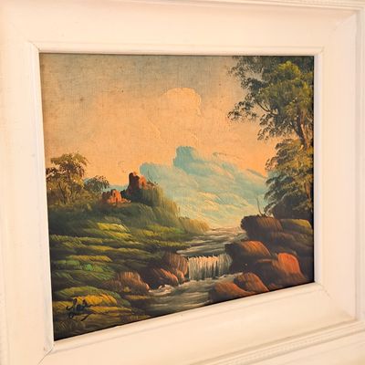 Sale Photo Thumbnail #35: Vintage landscape oil painting on canvas board depicting a river and distant ruins, housed in a wide white wooden frame.